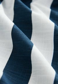 Pamukasti materijal s naizmjeničnim tamnoplavim i bijelim dijagonalnim prugama. Tekstura je glatka s suptilnim tkanim uzorkom.
