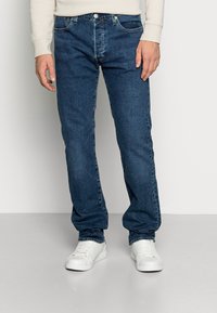 Mörkblå denimjeans med rak passform, med knapplås och dragkedja samt femfickorsdesign, ihop med vita sneakers.