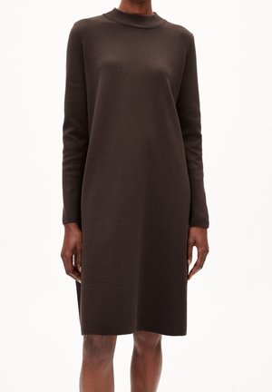 Ciemnobrązowa, dzianinowa sukienka z długim rękawem sięgająca do kolan, z wysokim dekoltem, noszona przez osobę stojącą na białym tle.