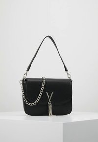 Černá kožená kabelka přes rameno s klopou, stříbrným řetízkovým popruhem, raženým logem a dekorativním řetízkem na přední straně.