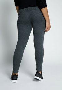 Grijze legging met een slimfit ontwerp, een gladde textuur en een brede tailleband, gecombineerd met zwarte sportschoenen met een witte zool.
