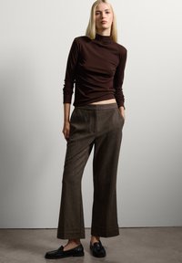 Bruine fitted coltrui gecombineerd met brede bruine tweed broek, voorzien van zakken en een omgeslagen zoom. Zwarte loafers maken de outfit af.