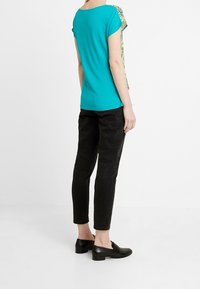 Camiseta turquesa de manga corta, con costuras laterales con estampado; pantalones ajustados negros; zapatos negros sin cordones; textura de tela suave.