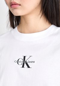 Witte katoenen t-shirt met een zwart geborduurd "CK" logo en de tekst "Calvin Klein Jeans". Klassiek ronde hals ontwerp en een gladde textuur.
