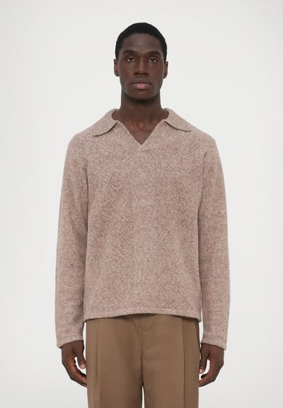 Pull en tricot marron clair avec un col large, motif en diamant texturé, et manches longues, associé à un pantalon beige.
