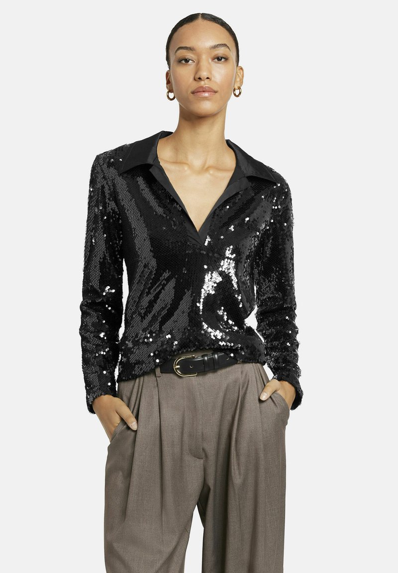 Schwarze Paillettenbluse mit Kragen und langen Ärmeln, die eine glänzende Textur aufweist, kombiniert mit hoch taillierten, gefalteten beigen Hosen.