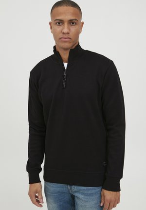 Zwarte zip-up sweatshirt met hoge kraag, ribgebreide manchetten en onderrand, met een gladde textuur. Draag het over een wit shirt, gecombineerd met denim.