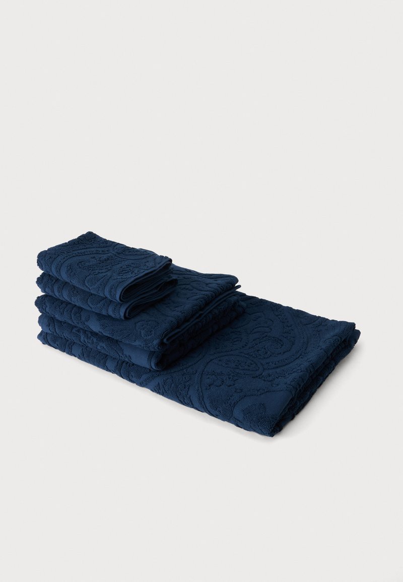 Pile de quatre serviettes bleu foncé pliées avec des motifs floraux en relief sur un fond gris clair.
