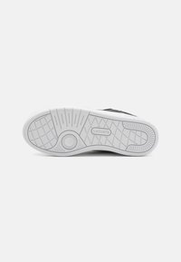 Sneaker nera con lacci, suola in gomma bianca testurizzata caratterizzata da un battistrada decorato e dettagli del logo in rilievo. Materiale superiore liscio.
