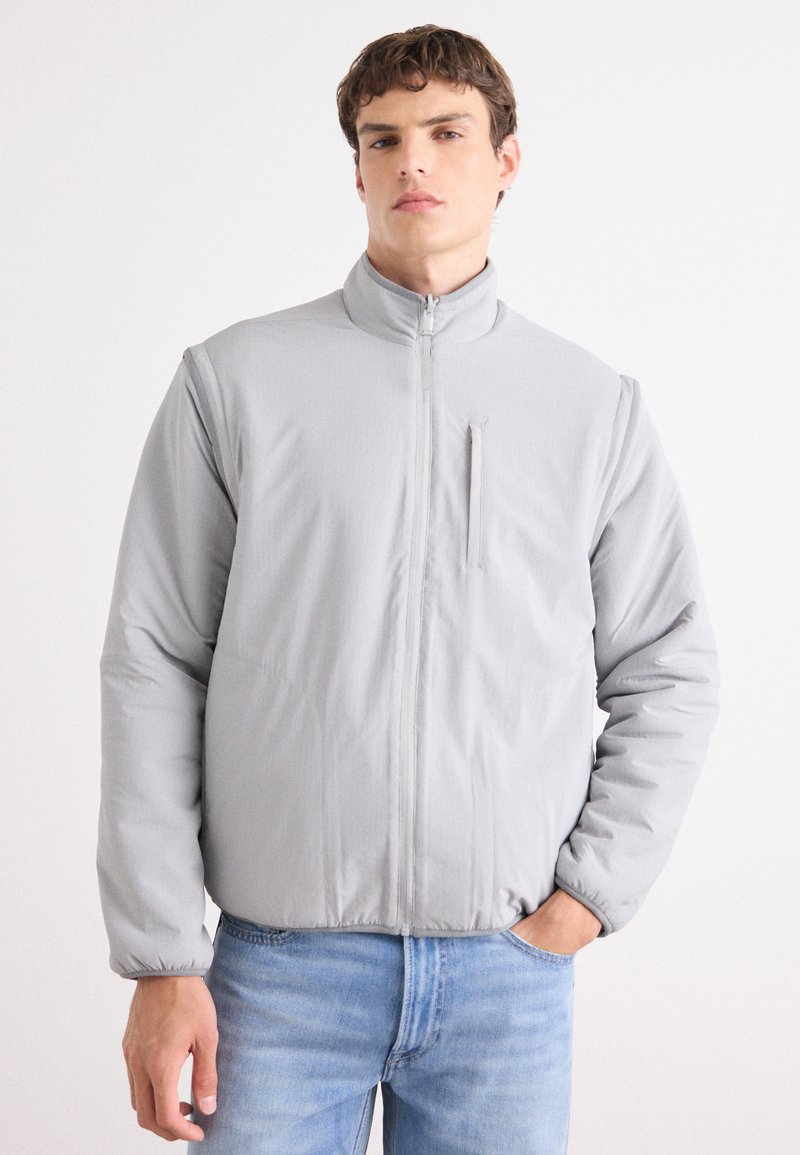 Lys grå, zip-up jakke med høy krage, med en frontlomme og ribbede mansjetter. Glatt stoff med et stilrent, puffete design.