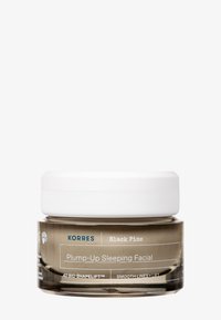 Korres Black Pine Plump-Up Sleeping Facial w przezroczystym słoiku z białą pokrywką; posiada okrągły kształt i nadrukowane etykiety na pojemniku.