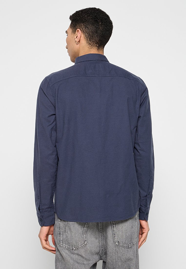 Marineblaues Langarmhemd mit Kragen, geknöpften Manschetten und abgerundetem Saum. Hergestellt aus glattem Stoff, mit einfarbigem Muster.