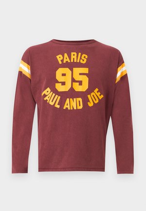 Chemise à manches longues bordeaux avec texte jaune "PARIS 95 PAUL AND JOE" et rayures blanches et jaunes sur le haut des manches.