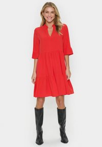 Robe rouge avec un design à volants, des manches trois-quarts à volants et un décolleté en V, accompagnée de bottes noires jusqu'aux genoux.