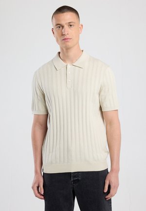 Lichtbeige polo shirt met korte mouwen, verticale ribbelstructuur, enkele rij knopen en een klassieke kraag. In combinatie met donkere spijkerbroek.