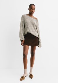 Hellgrauer Strickpullover mit schulterfreiem Design, kombiniert mit einem braunen Wildleder-Minirock und braunen spitzen Schuhen mit Schleifendetail.