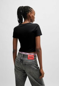 Black short-sleeve t-shirt paired with gray denim jeans featuring a pink and red branded waistband and a rectangular back patch.