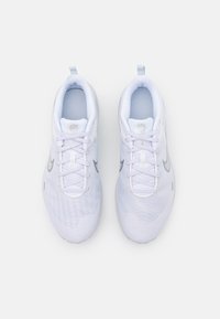 Une paire de baskets blanches en mesh, avec des logos Swoosh Nike gris et des lacets violet clair, placées côte à côte sur un fond blanc.