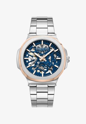 Zilveren roestvrijstalen horloge met een blauwe skeleton wijzerplaat, roségouden accenten en een zilveren armband. Beschikt over automatische beweging en gedurfde uurmarkeringen.