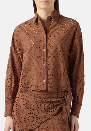 Bruin overhemd met knopen en bijpassende rok met ingewikkelde uitgesneden bloem- en geometrische patronen, gedragen door een persoon met handen langs het lichaam.