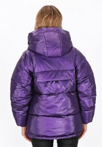 Lila puffertkabát fényes, steppelt textúrával. Kapucnival, elasztikus mandzsettával és hátsó zsebbel rendelkezik. Simább kivitel, laza fazonnal.