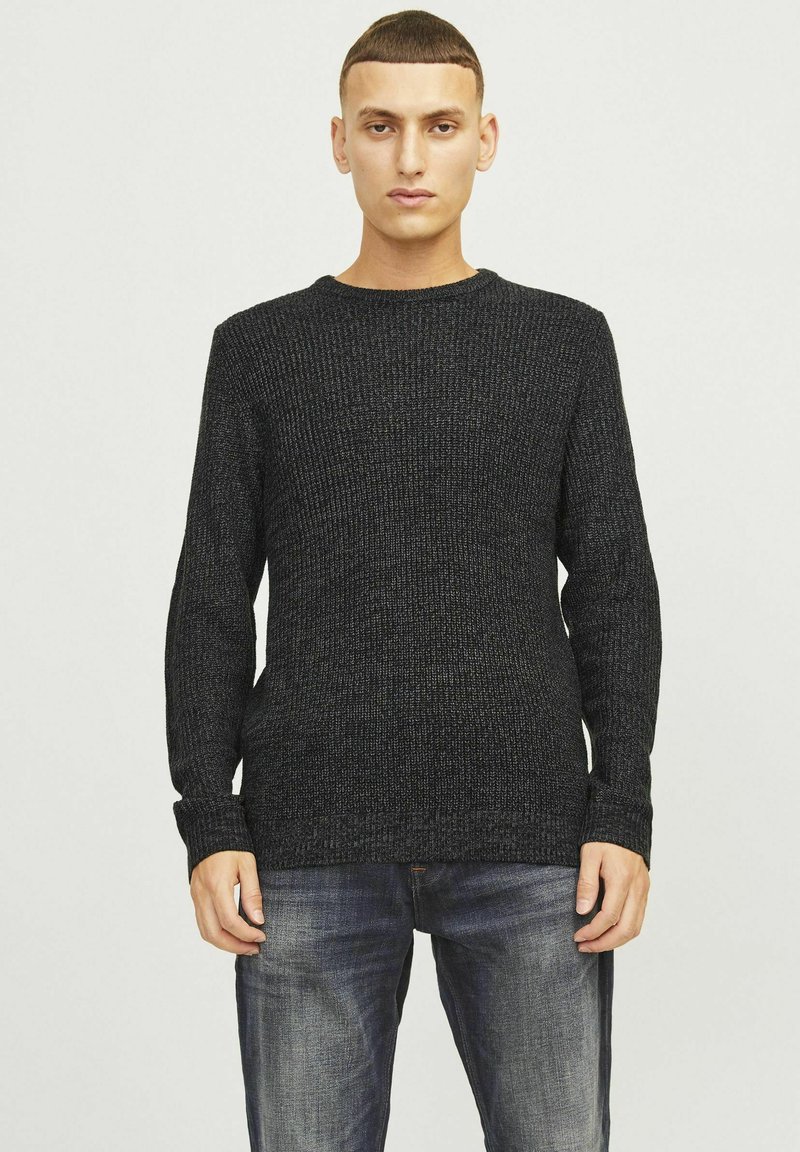 Schwarzer gestrickter Pullover mit rundem Halsausschnitt, langen Ärmeln und gerippter Textur. Kombiniert mit blauen Jeans.