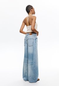 Jasnoniebieskie dżinsy o szerokich nogawkach z wyblakłym wykończeniem, pięcioma kieszeniami i brązową skórzaną łatą przy pasie. Połączone z dopasowanym topem z szydełka.