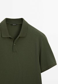 Tmavě zelené polo tričko z texturované látky, s žebrovaným límečkem, krátkými rukávy a předním zapínáním na tři knoflíky.