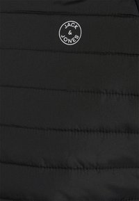 Giacca nera imbottita con cuciture orizzontali, caratterizzata da un logo bianco rotondo che recita "JACK & JONES" sul davanti. Texture liscia.