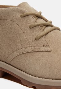 Chaussure en daim beige avec une tige texturée, un bout rond et des lacets assortis. Dispose d'une semelle en caoutchouc épaisse pour une meilleure adhérence.