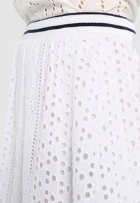 Gonna bianca in tessuto eyelet con ritagli circolari, superficie testurizzata e un elastico in vita a righe navy a contrasto.