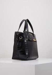 Černá kožená taška s krokodýlím vzorem, se zlatými akcenty, dvojitými horními uchy a pevným tvarem. Disponuje zipovým uzavřením a bočním kroužkem.