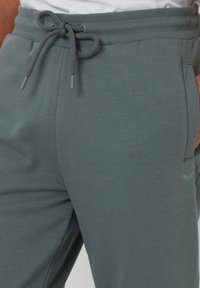 Dunkelgraue Jogginghosen aus weichem Stoff, mit einem Kordelzugbund und Seitentaschen. Dezentes Logodetail am unteren Bein.