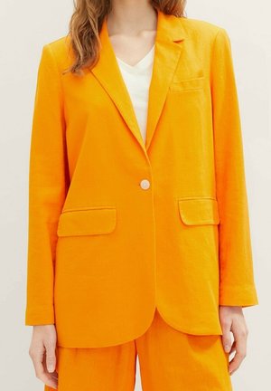 Oranssi bleiseri, jossa on yksittäinen nappikiinnitys, uurrettu kaulus ja kaksi etutaskua. Valmistettu kevyestä kankaasta, jossa on hieman strukturoidun tuntu.