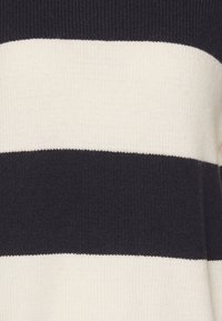 Pull en tricot avec des rayures horizontales noires et crème. Texture douce avec un col et un ourlet côtelés. Couleurs unies sans motif.