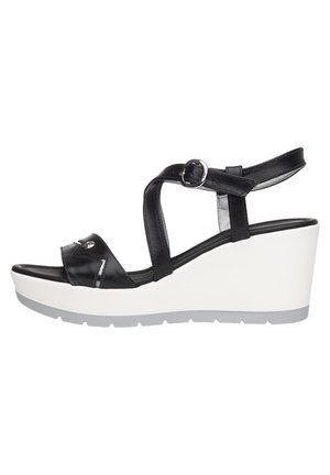 Czarna skórzana sandałka na koturnie z paskiem na kostkę zapinanym na klamrę oraz białą podeszwą na platformie.