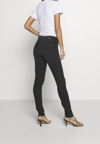 Jeans skinny negros con una textura suave, cintura alta y bolsillos traseros. Llevados con una camiseta blanca sencilla y sandalias de tacón con tiras.