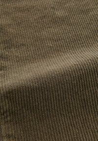 Tessuto di velluto a coste marrone con una texture a coste, che mostra strisce verticali. Superficie morbida con una sensazione leggermente pelosa e un colore tenue.