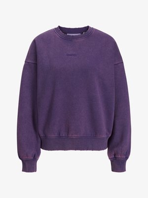 Lágy anyagból készült lila pulóver, kerek nyakkivágással, bordázott mandzsettákkal és szegéllyel, a közepén diszkrét márkázással.