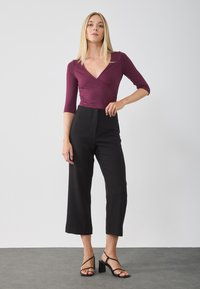 Burgundy wrap top with three-quarter sleeves, paired with high-waisted black cropped trousers and black block-heeled sandals.