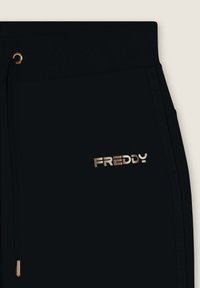 Pantalones de chándal negros con un logo dorado "FREDDY". Presentan una cinturilla acanalada y cordón, con branding en los laterales. Textura suave en toda la prenda.