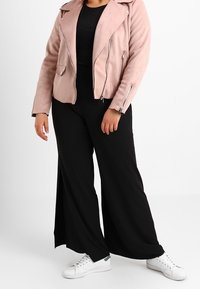 Różowy zamszowy kurtka typu biker z zamkami błyskawicznymi, noszona na czarnej bluzce i szerokich czarnych spodniach, zestawiona z białymi trampkami.