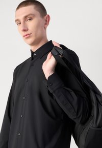 Svart knapp-up skjorte med klassisk krage, glatt tekstur og lange ermer, kombinert med en stilren svart veske med justerbare stropper.