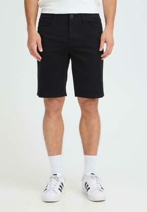 Sorte denimshorts med knaplukning foran, to forlommer og lige snit, kombineret med hvide sokker og sneakers med sorte striber.