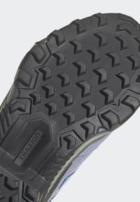 Suola esterna in gomma nera con tacchetti multidirezionali, motivi testurizzati e marchio "TRAXION" per una maggiore aderenza e trazione.