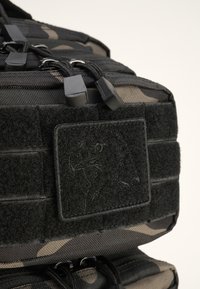 Kamikazės maišas su juodais akcentais, tekstūruotas Velcro pleistras, juodos užtrauktukai ir elastinės virvės. Pasižymi tvirta medžiaga ir struktūrizuotu dizainu.