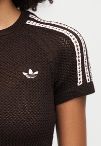 Top marrón de manga corta tejido con un logo blanco bordado en el pecho izquierdo y rayas rosas a lo largo de los hombros. Diseño texturizado.