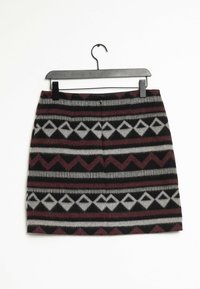 Mini-rok met geometrische diamanten en zigzagpatronen in zwart, grijs en donkerrood, hangend aan een zwarte hanger tegen een witte achtergrond.