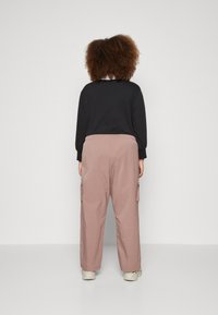 Chemise noire à manches longues et pantalon cargo rose clair avec poches latérales. Le pantalon a une coupe décontractée et une taille à cordon, associé à des chaussures légères.
