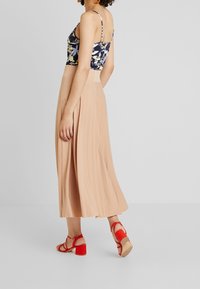 Top corto floreale in blu navy e giallo abbinato a una lunga gonna plissettata beige e sandali con tacco a blocco rossi. Tessuto morbido e vestibilità casual.